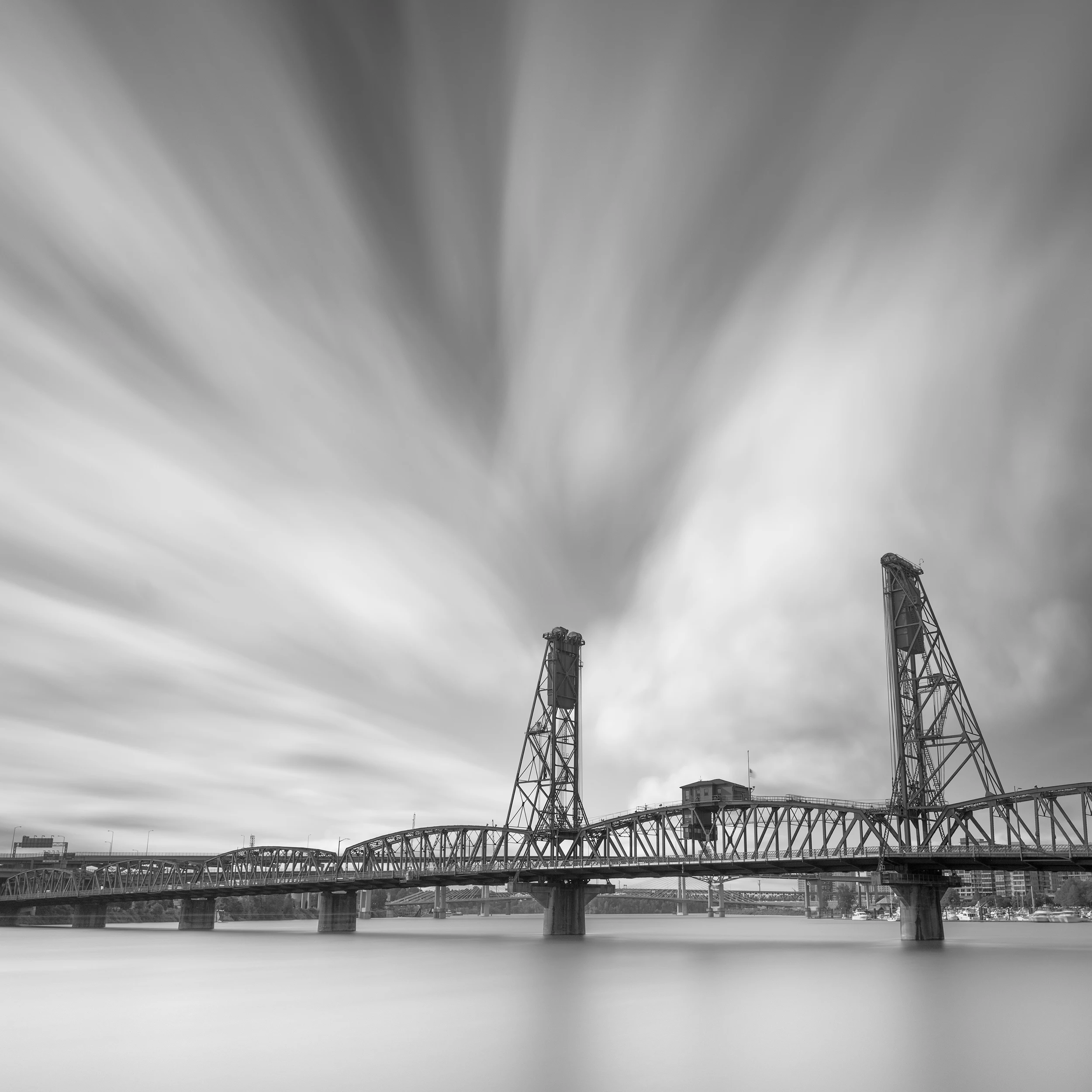 Black and white long exposure photograph of Hawthorne Bridge in Portland Oregon with dramatic streaking clouds and smooth water reflections