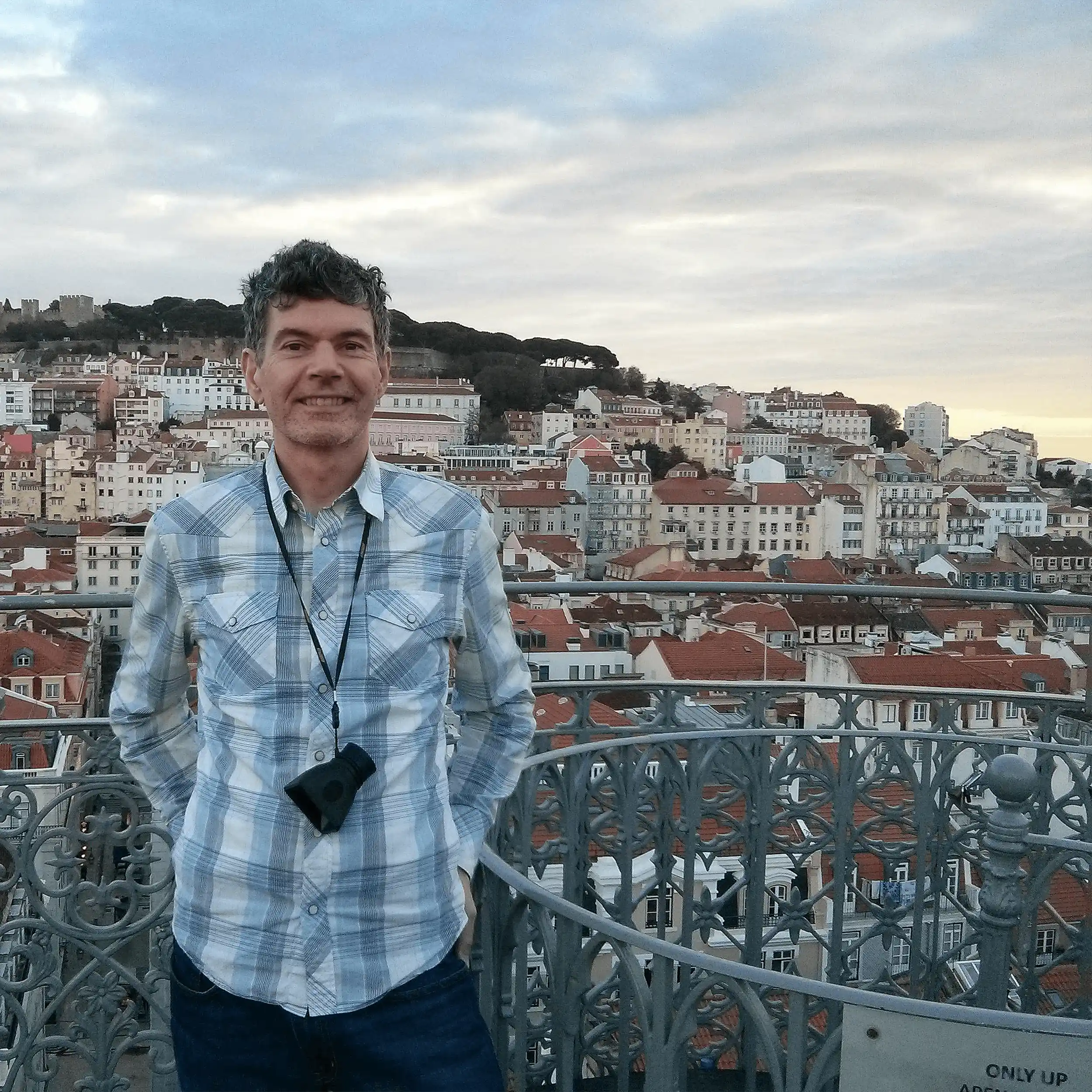Mark McCarvill standing on Santa Justa Lift observation deck with Lisbon cityscape and castle in background
