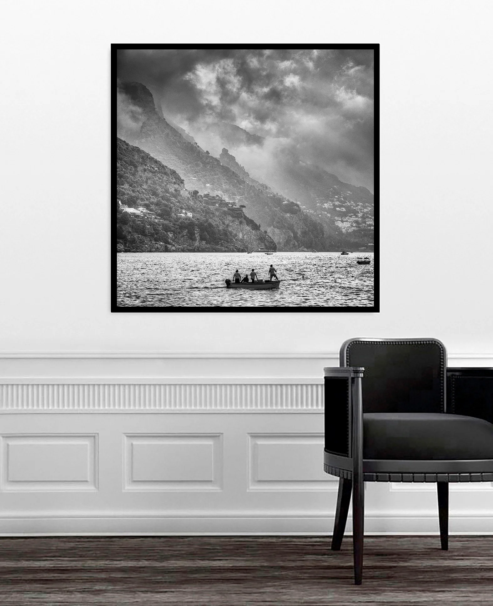 Black and white landscape photograph of fishing boat on water with dramatic coastal mountains and buildings in Positano Italy displayed in modern interior